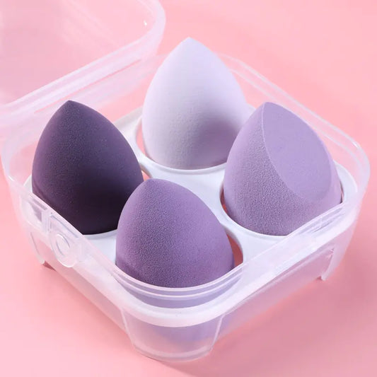 Four purple makeup sponges in a clear plastic container on a pink background