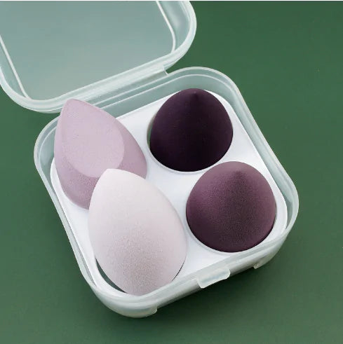 Four makeup sponges in a clear plastic case on a green background