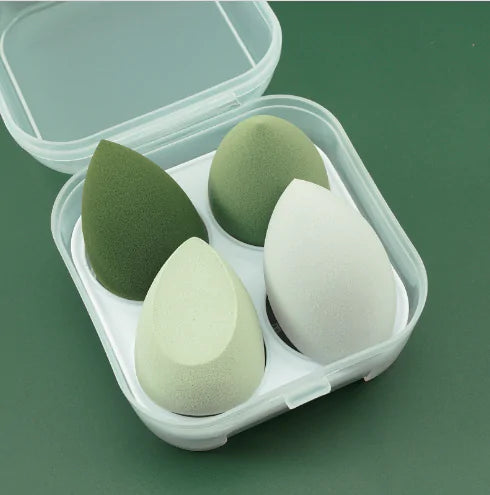 Set of green and white makeup sponges in a clear case on a green background