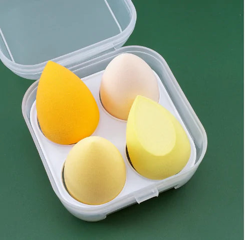 Four yellow and one beige makeup sponges in a clear container on a green background