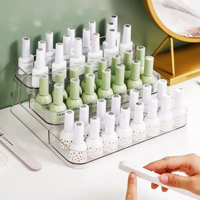 Nail polish bottles in a clear organizer on a white surface with a green wall background.