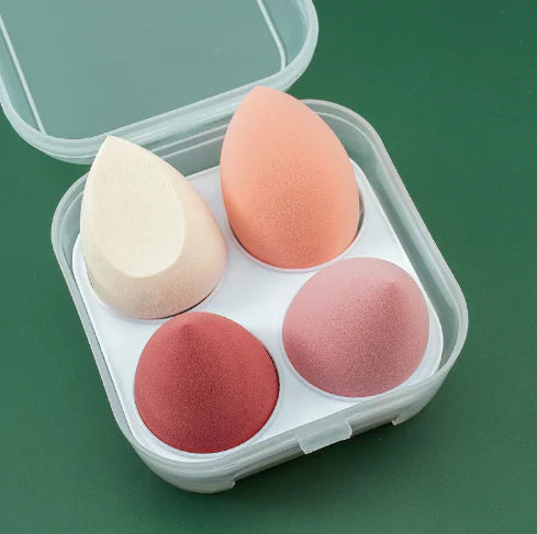 Four makeup sponges in a clear plastic case on a green background