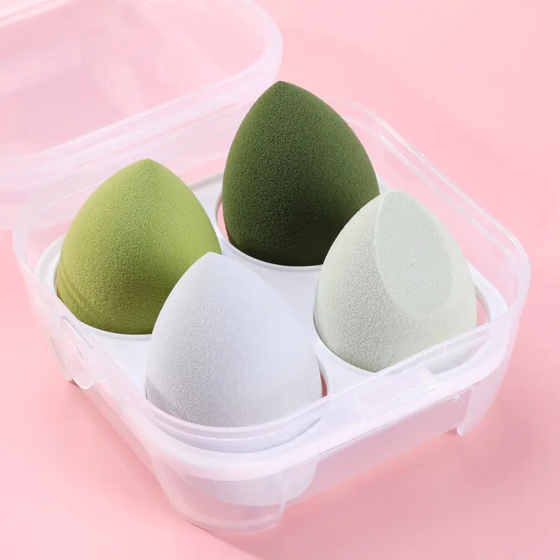 Four green and gray makeup sponges in a clear container on a pink background