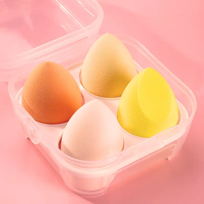 Four colorful makeup sponges in a clear container on a pink background